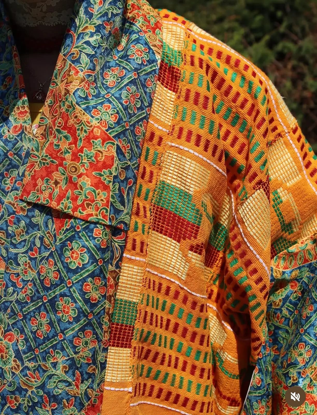 Close-up of Tanowa Tomiyama textiles: blue floral-embroidered fabric beside orange, green and red kente-style weaving.